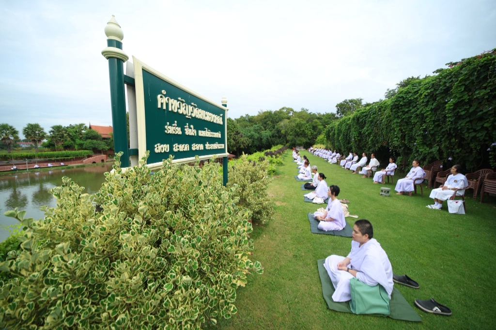 ผู้ปฏิบัติธรรมนั่งเจริญสมาธิเรียงรายบนสนามหญ้ารอบสระน้ำ